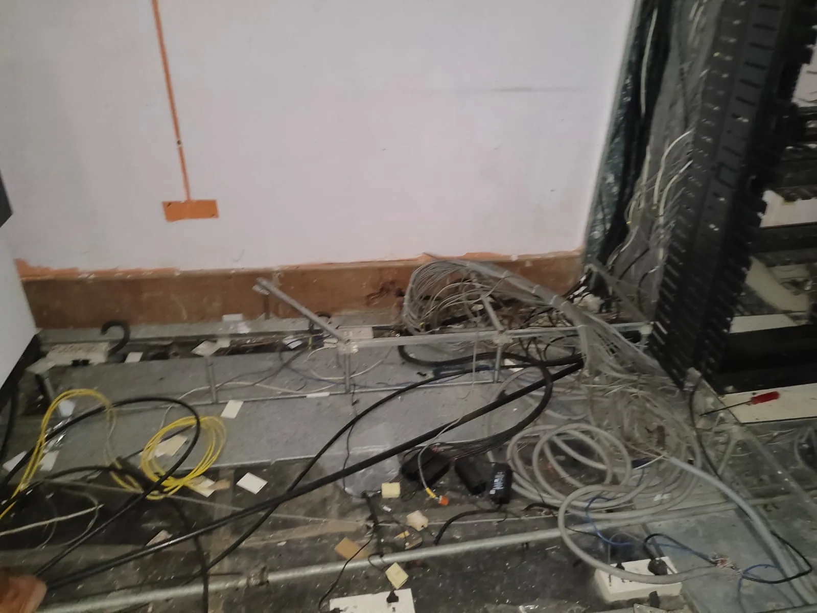 Exposed network cabling clusters, server racks, and power lines bundle on a raised floor grid during an IT office decommissioning service in Whitefield, Bengaluru.