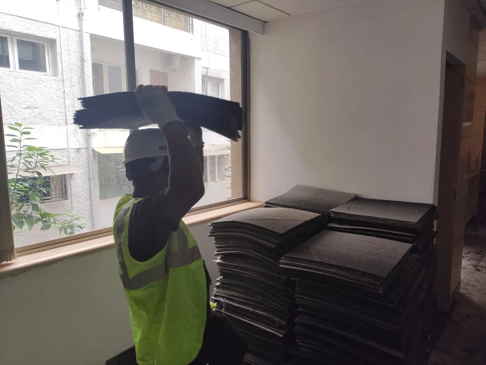 Professional technician wearing a safety helmet and high-visibility vest removing and stacking office carpet tiles during an office dismantling and lease reinstatement service in Whitefield, Bengaluru